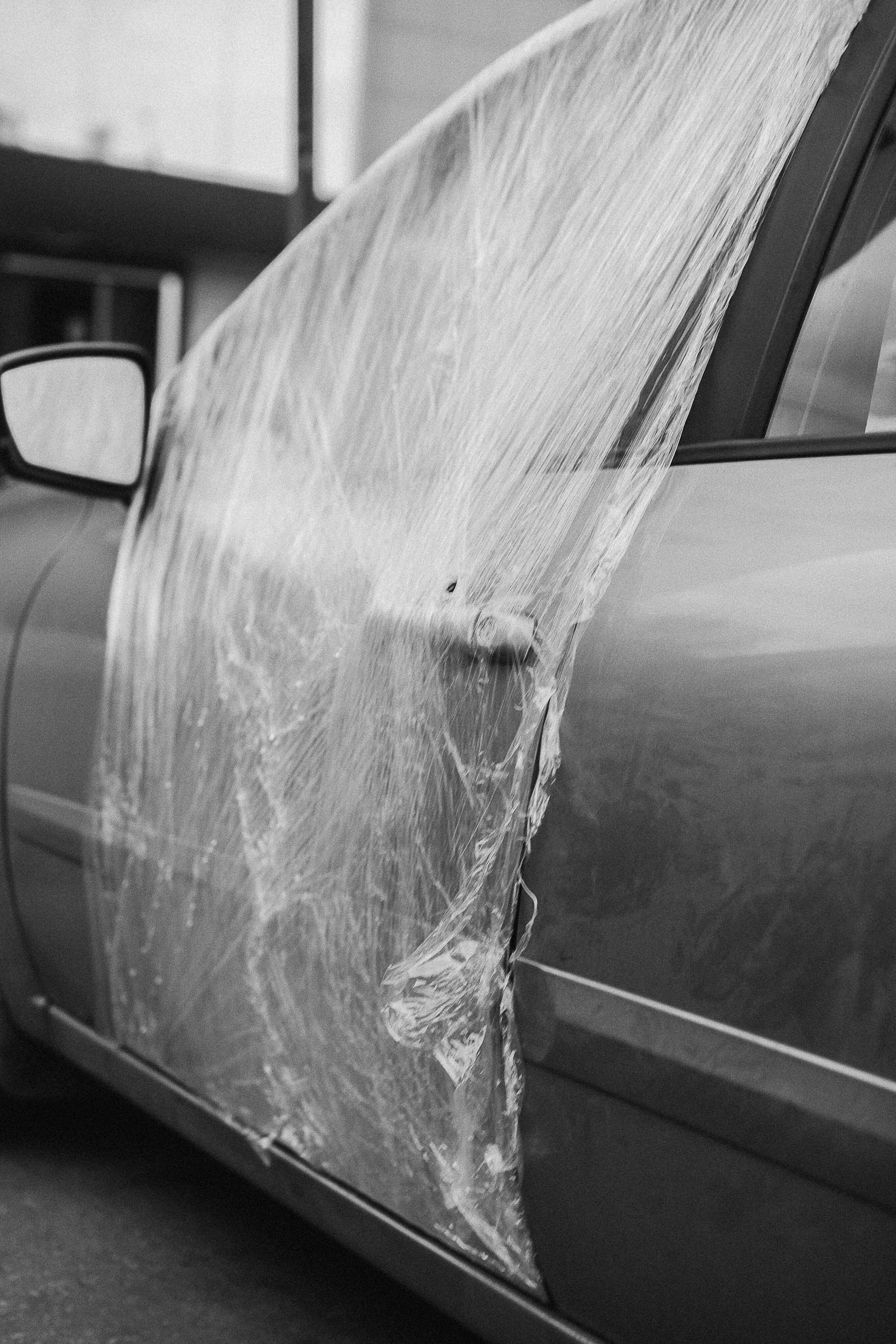 Black and white photo of a car door wrapped in plastic for repair
