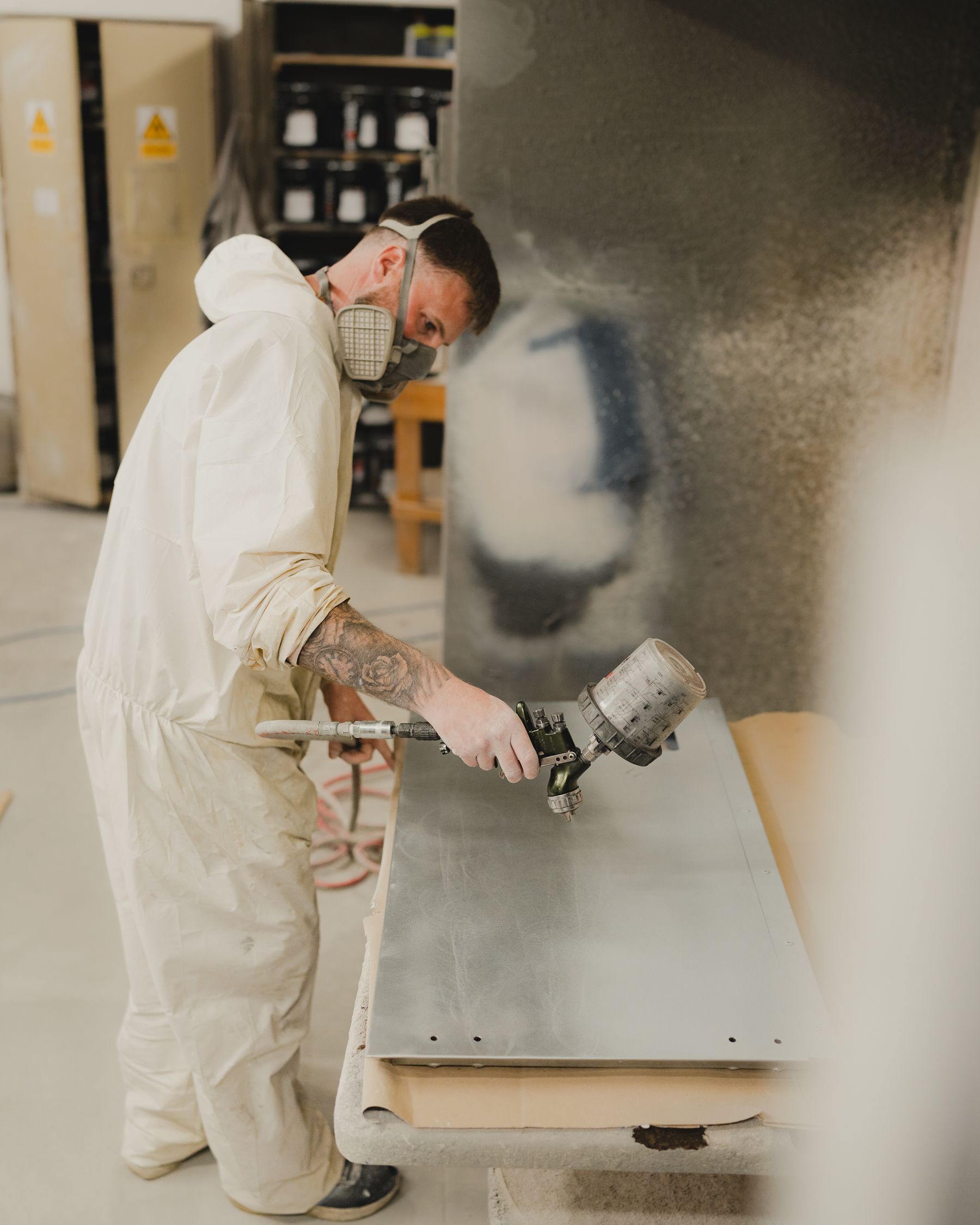 Painter in a protective suit spraying a metal panel